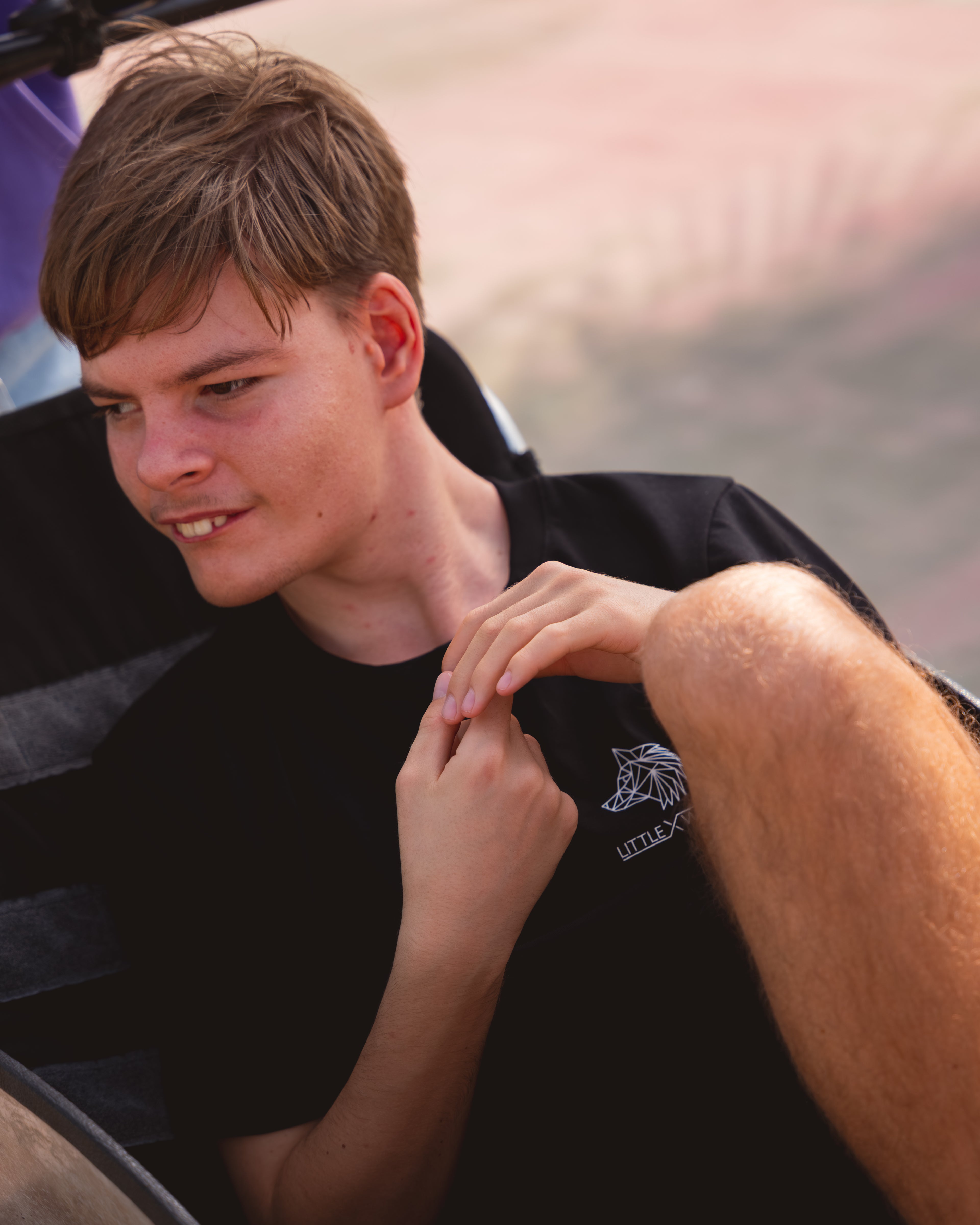 Rio wearing a black t-shirt with a LittleXWolf logo, sitting outdoors.