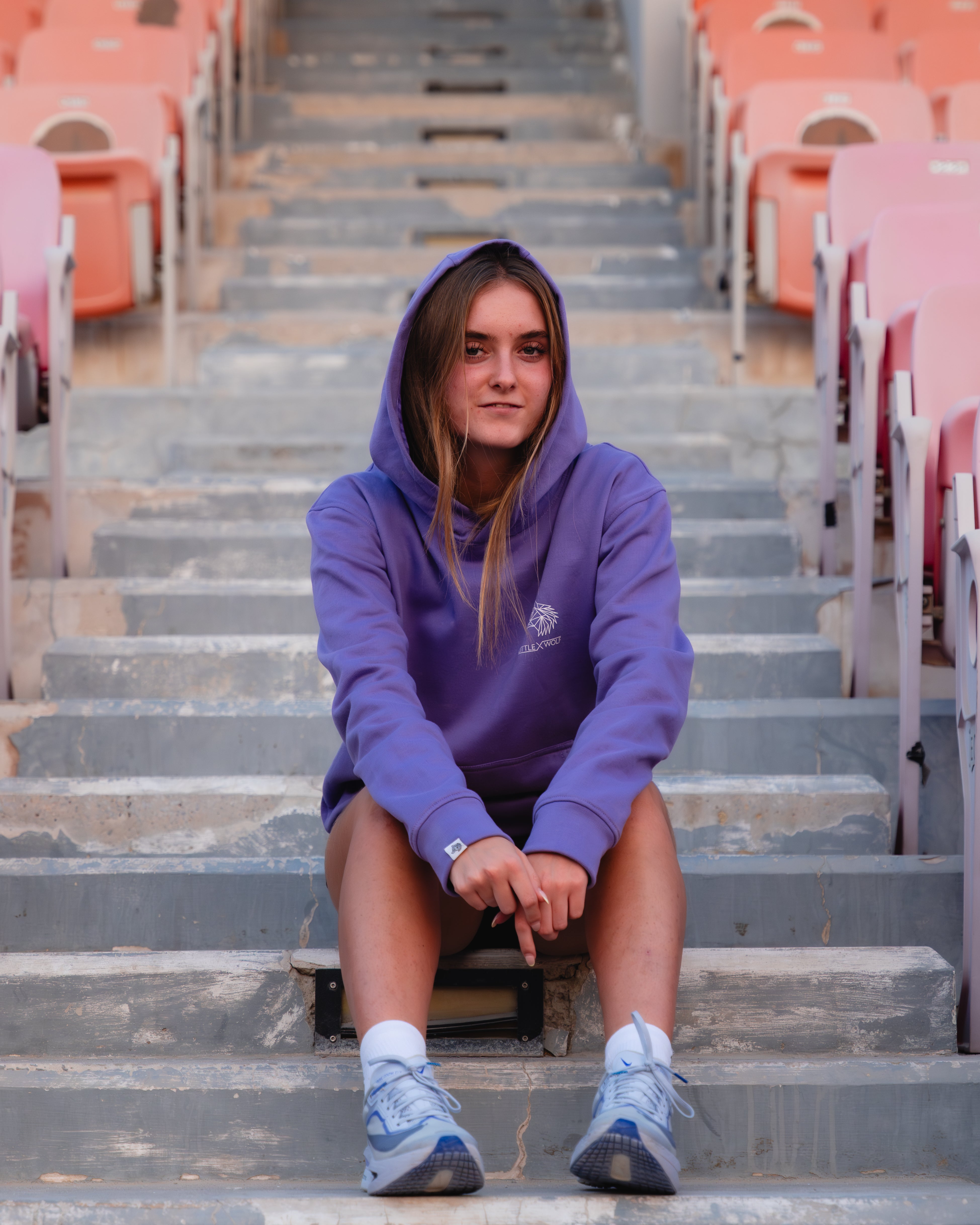 Tia wearing a purple hoodie sitting on stadium steps.