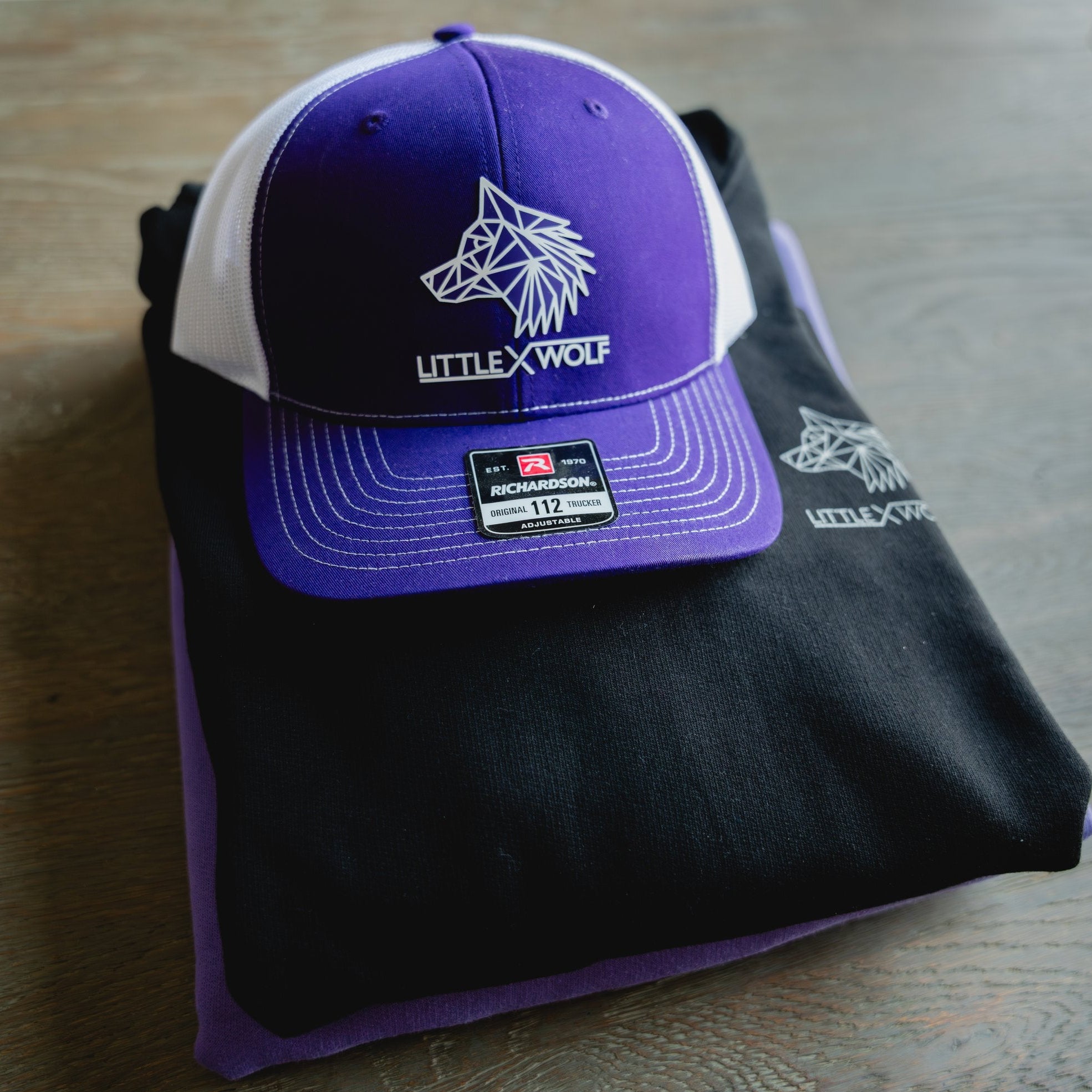 Purple and white cap with 'LITTLE WOLF' logo on a black t-shirt.