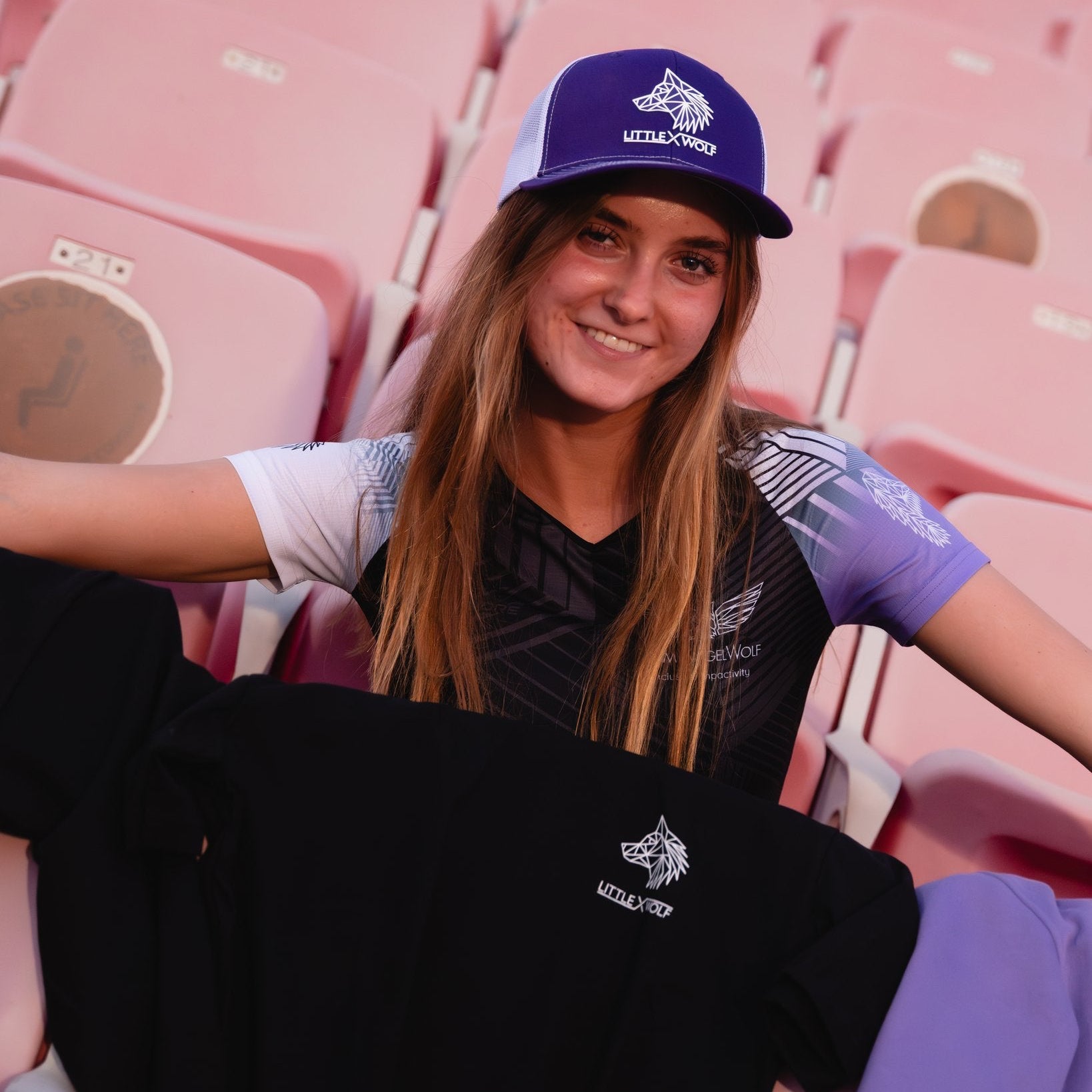 Tia wearing purple and white cap with LXW logo, sitting in red stadium seats.