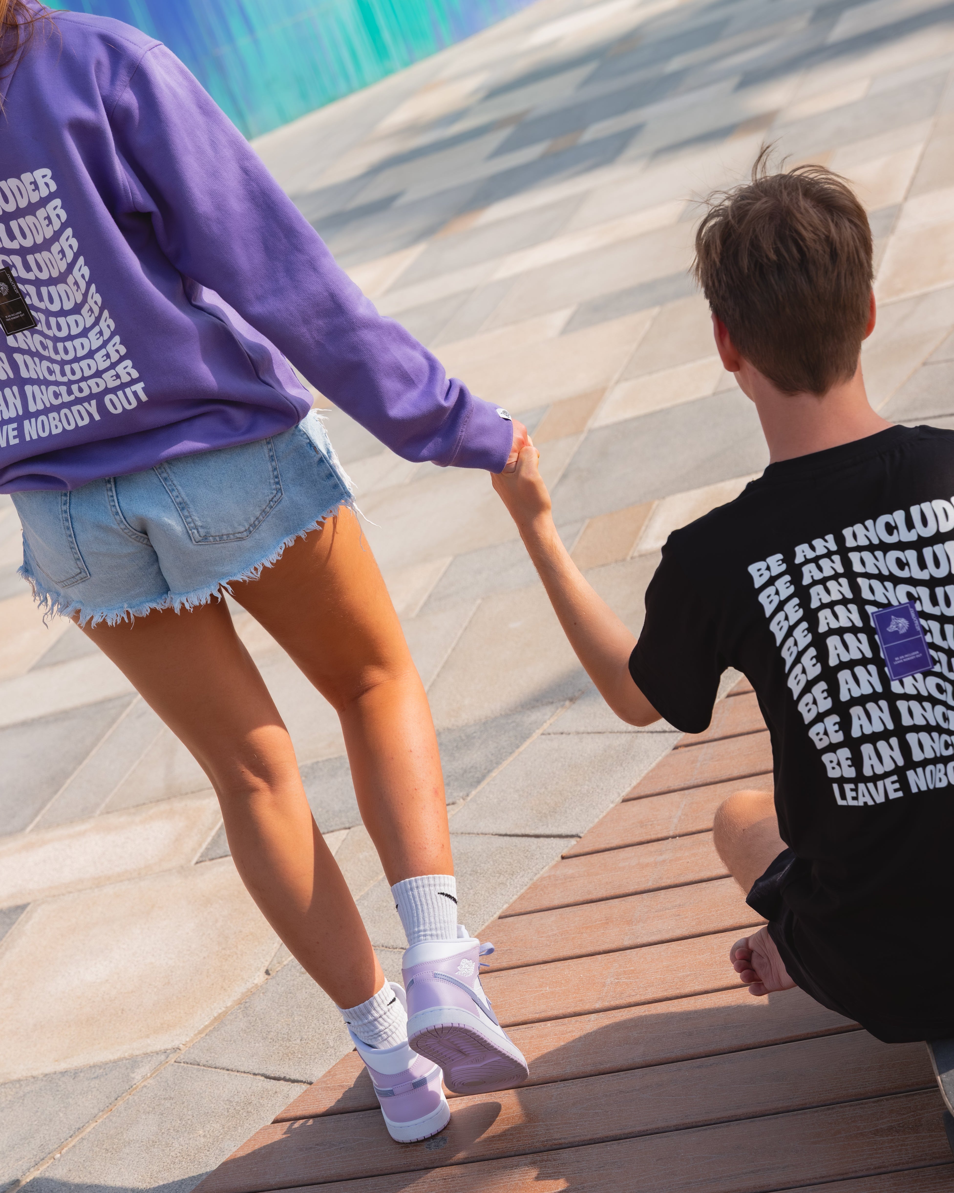 Rio & Tia holding hands on a skateboard with a colorful mural in the background.
